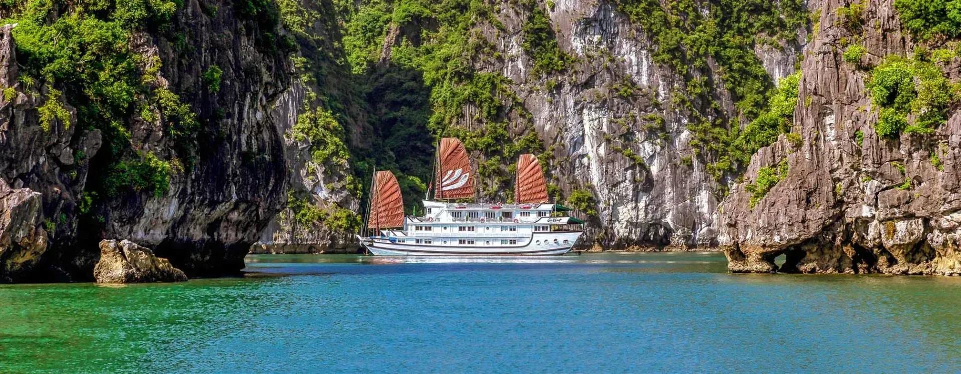 Bhaya Cruise navigating among lush limestone cliffs in Ha Long Bay.