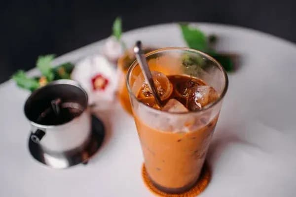 A glass of Vietnamese iced milk coffee with appealing color and delicious taste, accompanied by a traditional coffee filter.