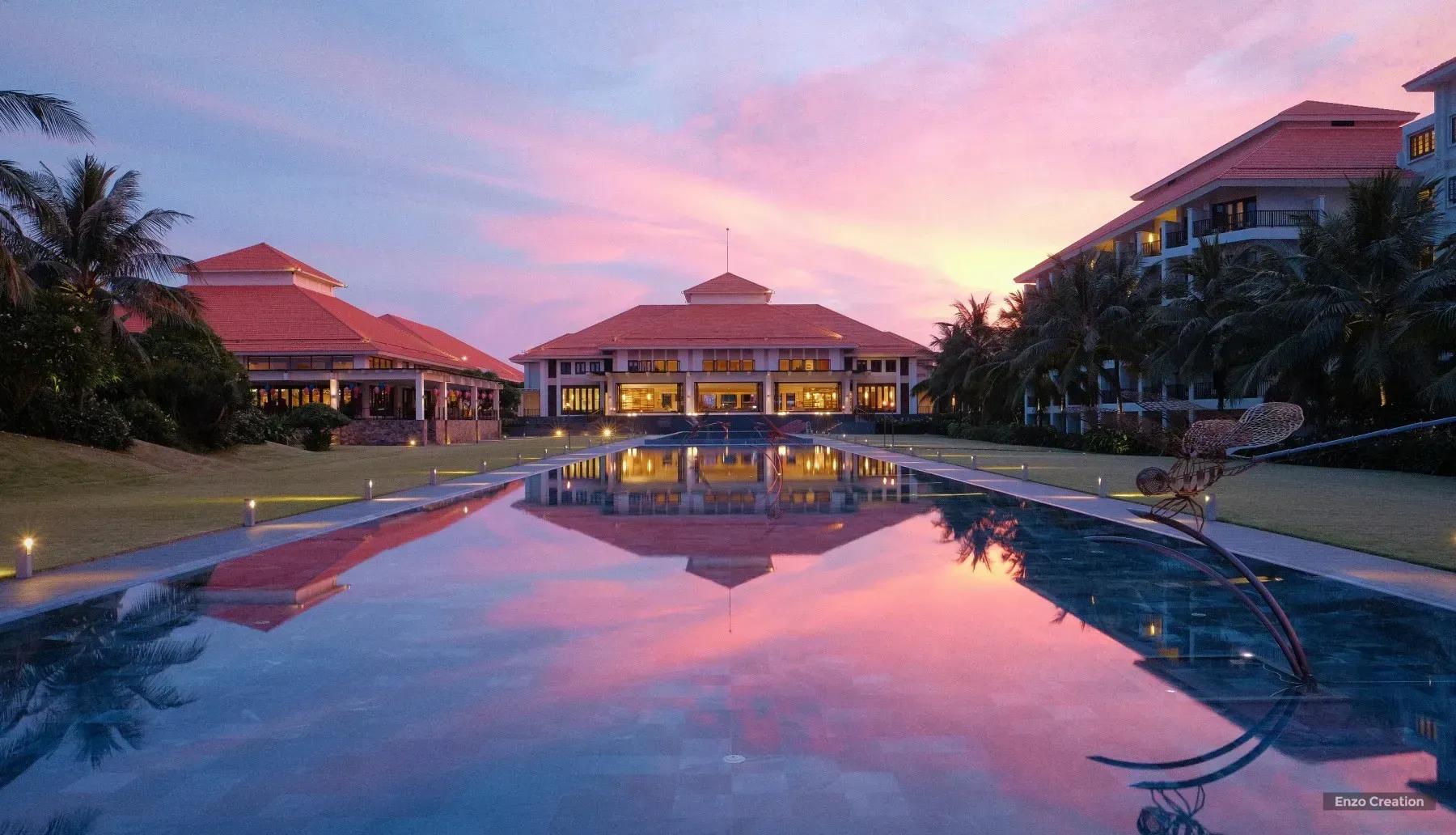 Luxury hotel with a long pool reflecting the vibrant sunset sky.